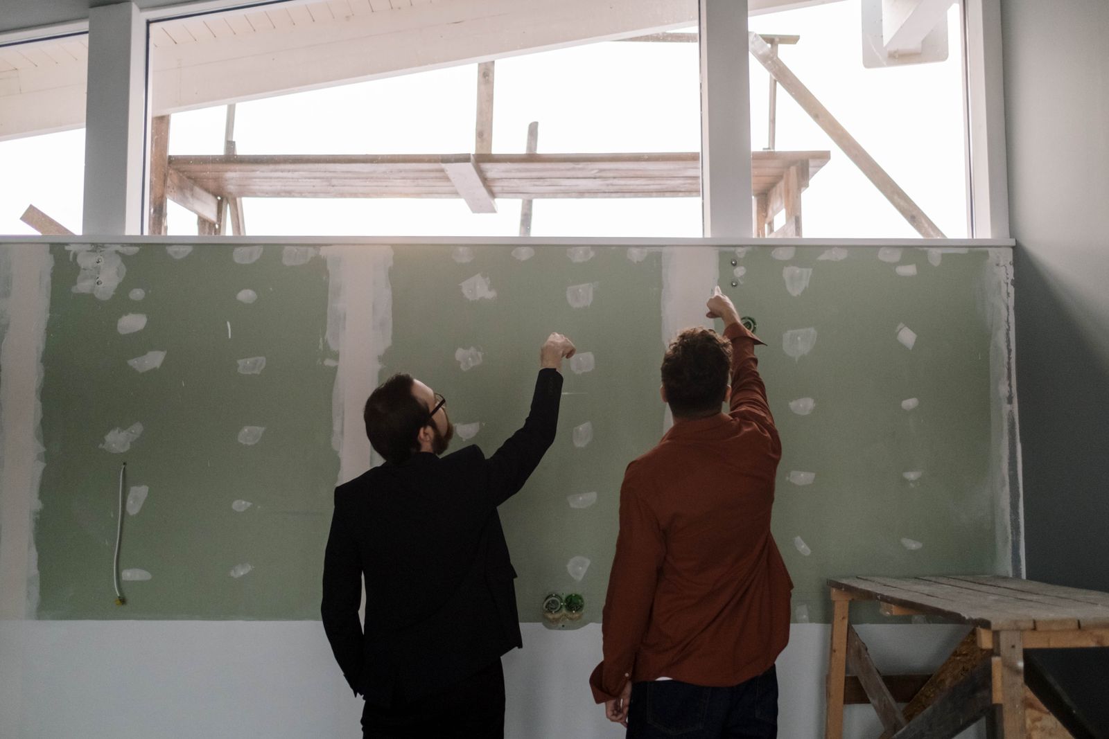 Chantier de rénovation avec mur mal enduit et documents de litige posés sur une table en bois